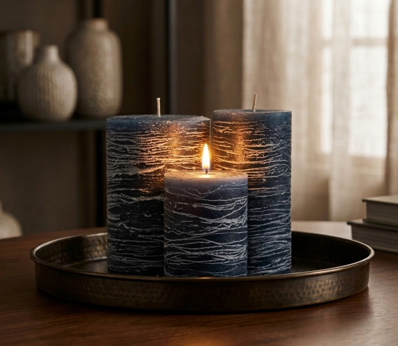 Three textured candles on a metal tray with a warm glow, set against a softly blurred indoor background.