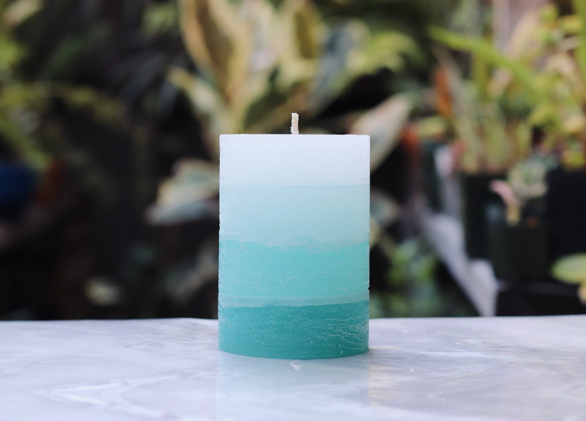 Gradient turquoise candle on a marble surface with a blurred natural background